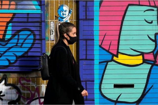 woman in mask walking in front of graffiti, Getty images