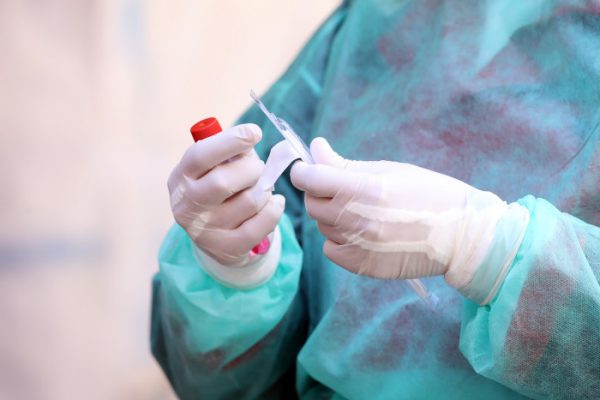 person in gloves and apron holding coronavirus test