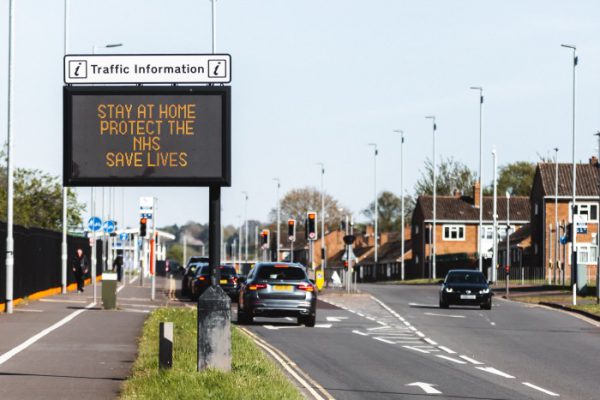 Busy road with sign saying 'Stay home, protect the NHS, save lives'