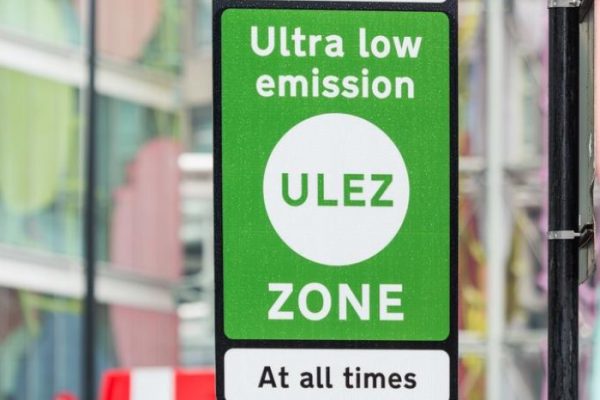 Green sign with white text reading 'Ultra low emission zone'. Smaller black text on white background 'At all times'