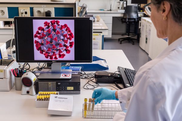 scientist in front of computer screen with image of coronavirus on monitor