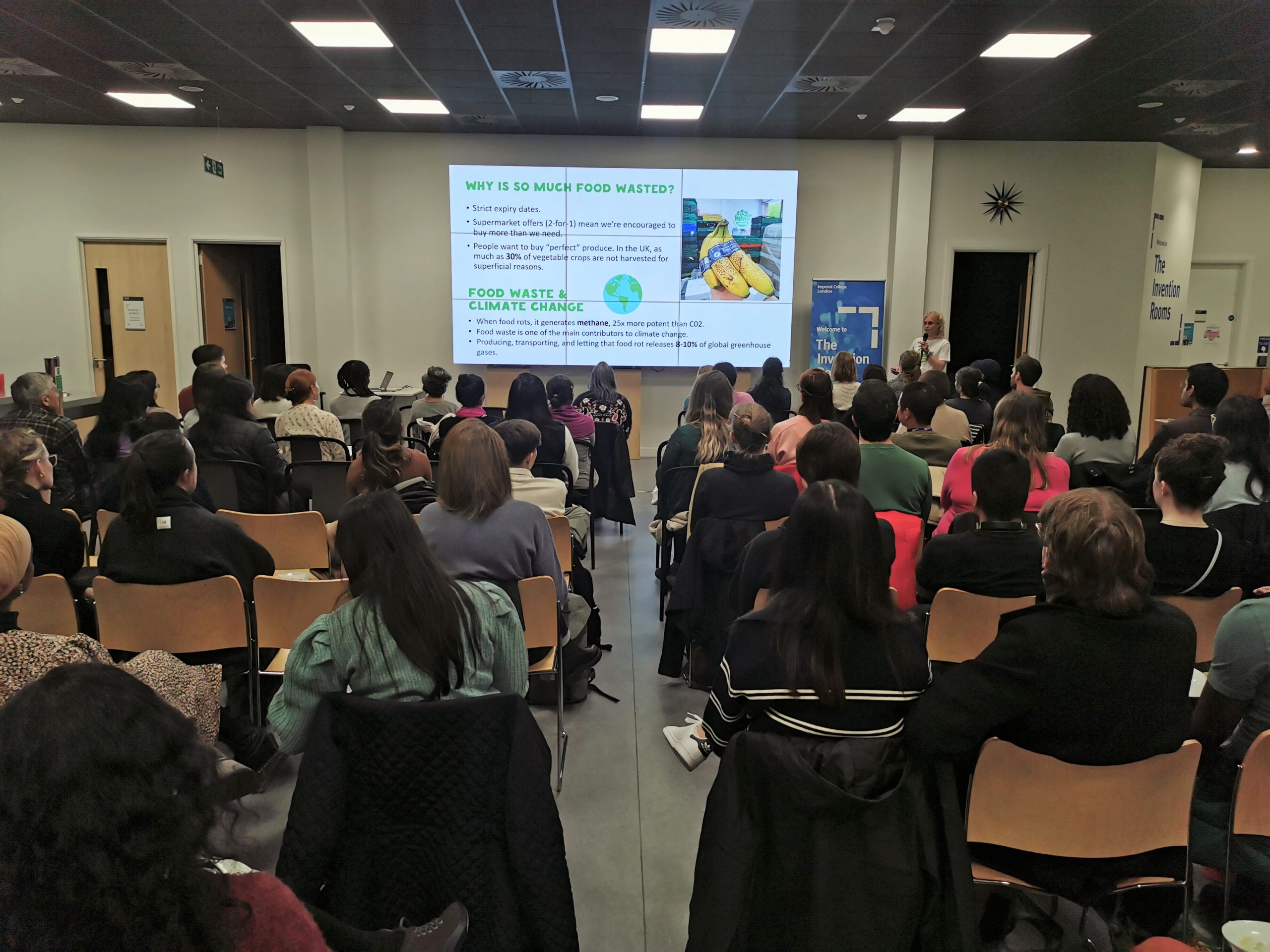 Woman from City Harvest sharing a powerpoint slide about food waste to a large audience.